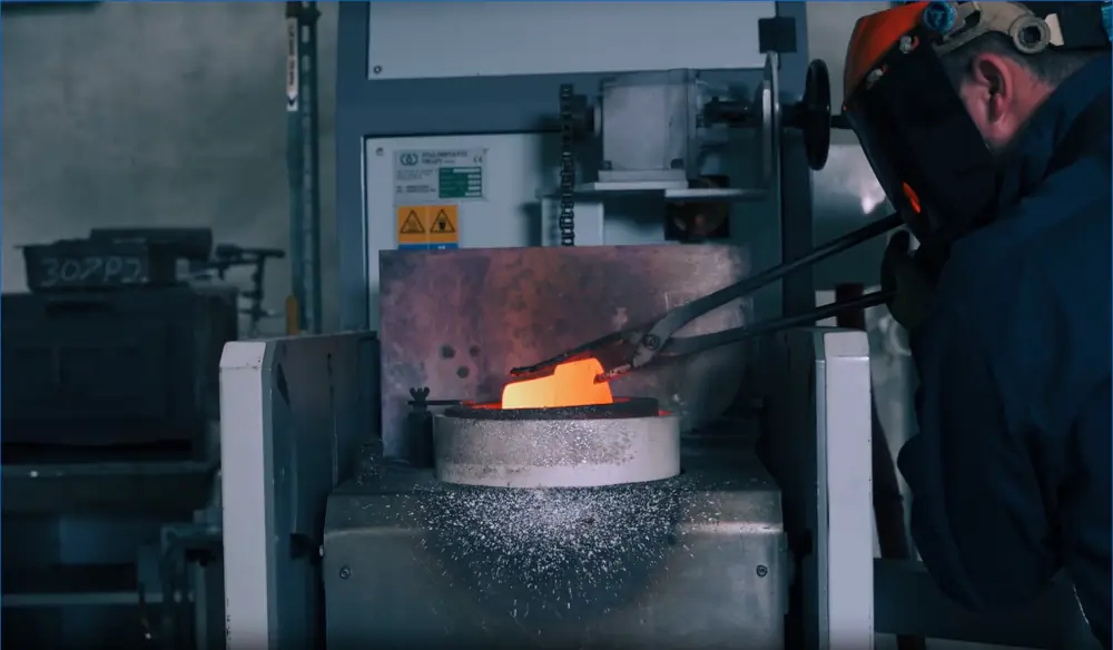 Refinery operator in a face shield lifting a crucible from an induction furnace